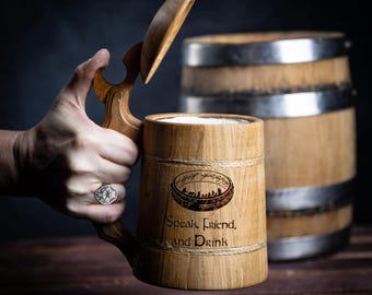 May include: A wooden beer stein with a lid and a handle. The stein is decorated with a rope design and the words "Speak, Friend, and Drink". The stein also features a graphic of the One Ring from The Lord of the Rings.