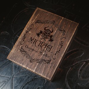 Puede incluir: Una caja de madera marr&oacute;n oscuro con un dise&ntilde;o decorativo y el texto "Michael Dungeon Master" grabado en la parte superior.