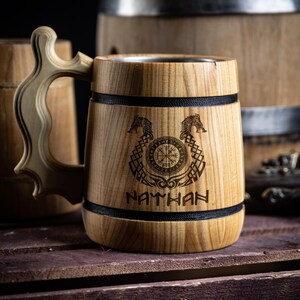 May include: A wooden beer stein with a stainless steel interior. The stein is engraved with a compass, two dragons, and the name "NATHAN".
