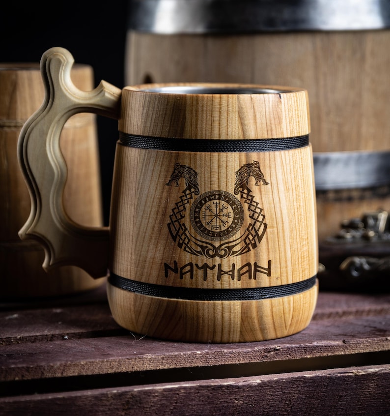 May include: A wooden beer stein with a stainless steel interior. The stein is engraved with a compass, two dragons, and the name "NATHAN".