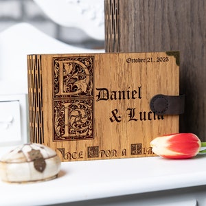 May include: A wooden box with a leather strap and engraved initials "D" and "L" for Daniel and Lucia. The box is inscribed with the date "October 21, 2023" and the phrase "Once upon a time".