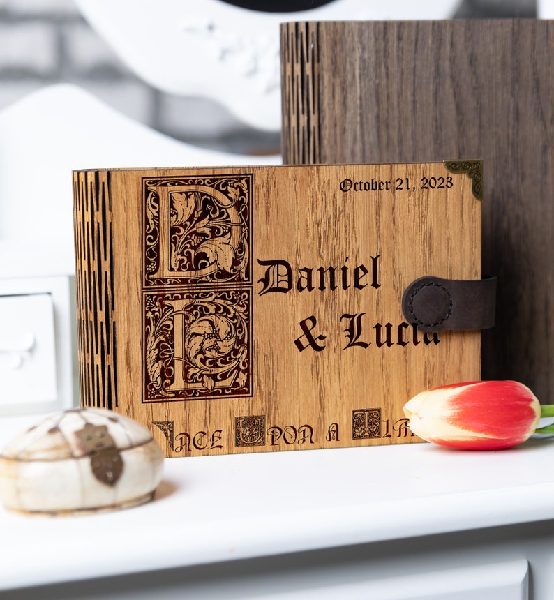 May include: A wooden box with a leather strap and engraved initials "D" and "L" for Daniel and Lucia. The box is inscribed with the date "October 21, 2023" and the phrase "Once upon a time".