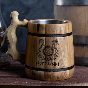 May include: A wooden beer stein with a stainless steel liner. The stein is decorated with a Viking compass, two wolf heads, and the name "NATHAN".