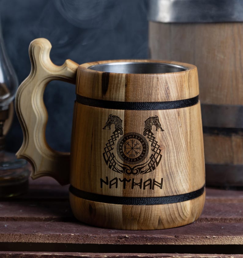 May include: A wooden beer stein with a stainless steel liner. The stein is decorated with a Viking compass, two wolf heads, and the name "NATHAN".