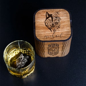 May include: A wooden box with a wolf design and the name "michael" engraved on the top. The box is next to a clear glass with a wolf design etched on the side.