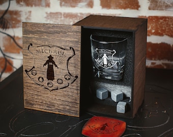 May include: A wooden box with a glass tumbler inside. The box is engraved with the name "Michael" and a design of a person in a robe. The tumbler is also engraved with the name "Michael" and a design of a person in a robe. The box includes a leather coaster with the name "Michael" engraved on it.