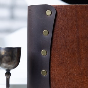 May include: A brown leather-bound journal with a dark brown leather flap and decorative brass rivets.