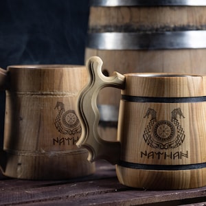 May include: Two wooden beer steins with black bands and engraved designs. The steins have the names "Nathan" and "NATH" engraved on them. The steins are sitting on a wooden surface.