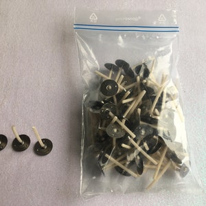May include: A bag of white candle wicks with black metal bases. Three wicks are shown outside of the bag.