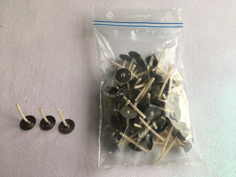 May include: A bag of white candle wicks with black metal bases. Three wicks are shown outside of the bag.