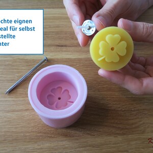 May include: A pink silicone mold with a four-leaf clover design. A yellow candle with a four-leaf clover design is being removed from the mold. The candle has a metal wick attached to the top.
