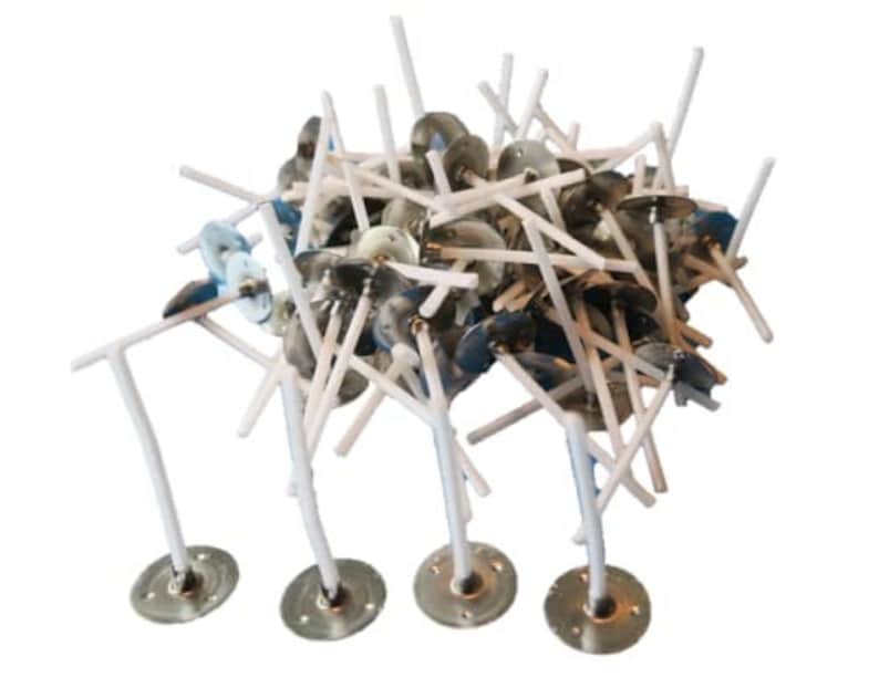 May include: A pile of white candle wicks with metal bases. The wicks are arranged in a random pattern and are all the same size. The bases are silver and have a small hole in the center.