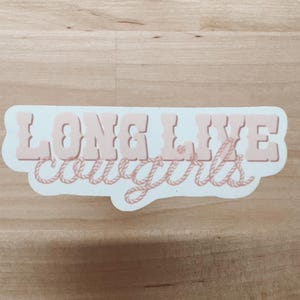 May include: White sticker with the text "LONG LIVE cowgirls" in pink lettering with a rope design around the words.
