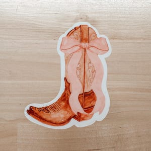 May include: A brown cowboy boot with a pink bow tied around the top. The boot is illustrated in a watercolor style.