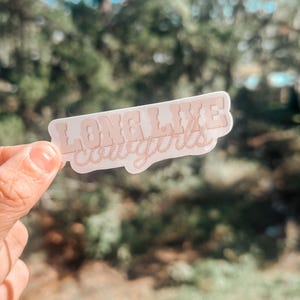 May include: A pink sticker with the text "Long Live Cowgirls" in a stylized font. The text is outlined with a rope design.