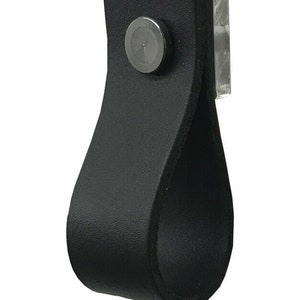 Pode incluir: Puxador de armário de couro preto com um parafuso de metal. O puxador tem a forma de um laço e um acabamento liso.