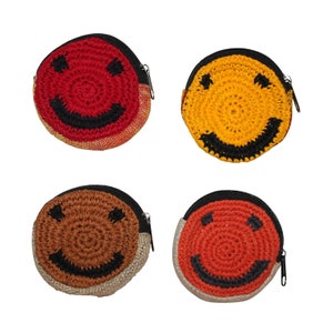 May include: Four crocheted smiley face coin purses in different colors. The purses are red, yellow, brown, and orange. Each purse has a black zipper.