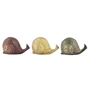 Peut inclure: Trois figurines de décoration en forme d'escargots dans différentes couleurs : rouge, or et vert. Chaque escargot a une coquille détaillée et un corps enroulé.