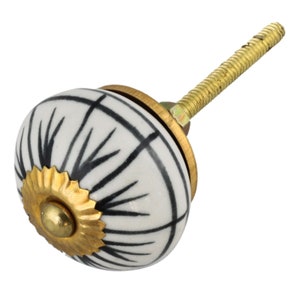 Könnte beinhalten: Weißer Keramik-Knopf mit geometrischem Muster in Schwarz und Weiß. Der Knopf hat eine goldene Metallbasis und eine Schraube.