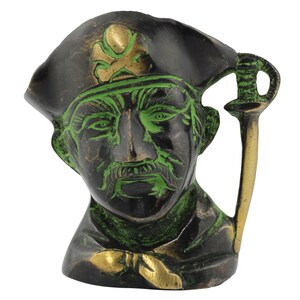 Könnte beinhalten: Eine grüne und goldene Piratenfigur aus Metall mit einem Schwertknauf. Der Pirat trägt einen schwarzen Hut mit einem goldenen Totenkopf und Knochenkreuz.