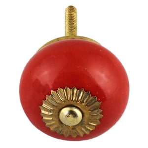 Op de afbeelding: Rode keramische knop met een gouden metalen basis en een decoratieve, gegolfde rand. De knop is ontworpen voor gebruik op kasten, lades of deuren.