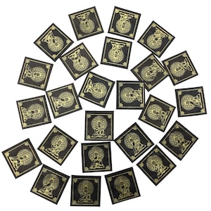 May include: A string of 20 black square prayer flags with gold printed designs of a seated figure with a mandala behind them. The flags are connected by a thin string.