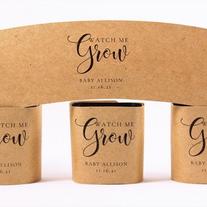 May include: Three brown paper seed packets with the text "Watch Me Grow" and "Baby Allison 11.16.21" printed on them.