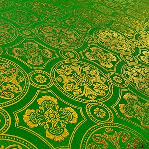 Puede incluir: Tela verde con un dise&ntilde;o estampado en dorado y rojo. El patr&oacute;n presenta c&iacute;rculos repetidos con una cruz en el centro.