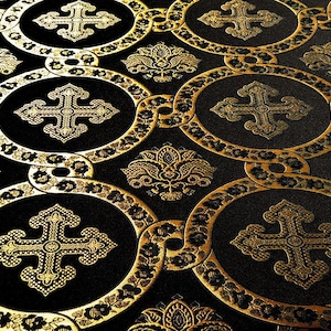 May include: Black fabric with a repeating pattern of gold crosses and floral designs. The fabric has a textured, woven look.