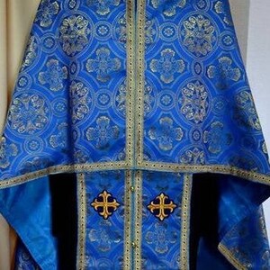 Puede incluir: Una vestimenta lit&uacute;rgica azul con bordados dorados y un dise&ntilde;o estampado. La vestimenta tiene un cuello y una t&uacute;nica larga y fluida.