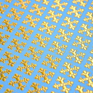 May include: A blue fabric with a repeating pattern of gold embroidered snowflakes.