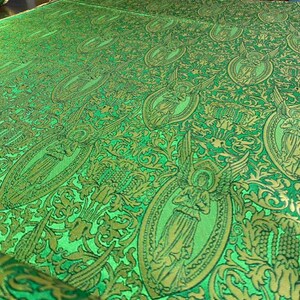May include: Close-up of a green fabric with a repeating pattern of angels in gold ovals. The fabric has a detailed, ornate design with floral and leaf motifs. The overall look is rich and textured.