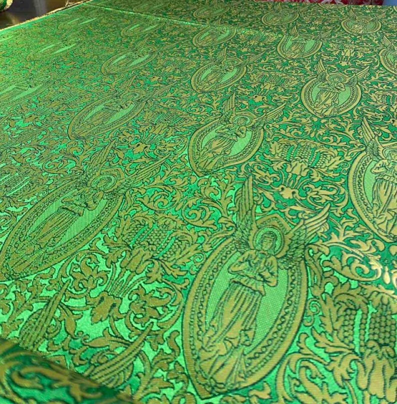May include: Close-up of a green fabric with a repeating pattern of angels in gold ovals. The fabric has a detailed, ornate design with floral and leaf motifs. The overall look is rich and textured.