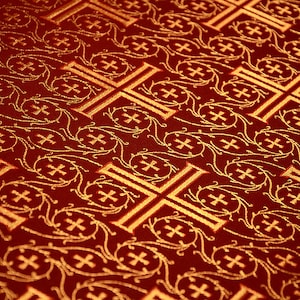 May include: Red fabric with a repeating pattern of gold crosses and floral designs.