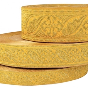 Op de afbeelding: Drie rollen gouden trim met een bloemen- en kruispatroon. De trim is gemaakt van een geweven stof met een reli&euml;fdesign.