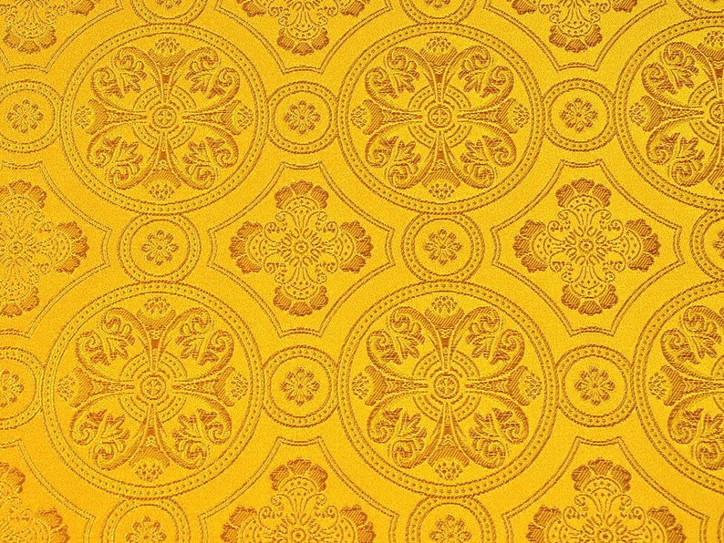 Puede incluir: Una tela amarilla con un patr&oacute;n repetitivo de intrincados dise&ntilde;os florales marrones. El patr&oacute;n es sim&eacute;trico y presenta un motivo en forma de cruz en el centro de cada dise&ntilde;o.