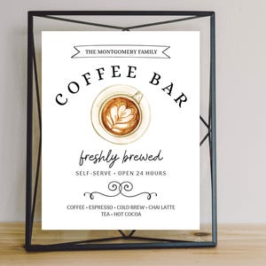 May include: A black framed sign with white text that reads "The Montgomery Family Coffee Bar" with a stylized image of a cup of coffee. The text below the image reads "freshly brewed, self-serve, open 24 hours". The bottom of the sign lists the coffee options: "Coffee, Espresso, Cold Brew, Chai Latte, Tea, Hot Cocoa."