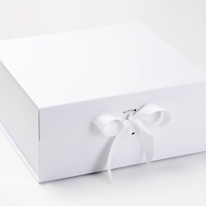 May include: A white, square gift box with a magnetic closure, tied with a white satin ribbon and bow. The box has a plain, minimalist design. Ideal for gifts.