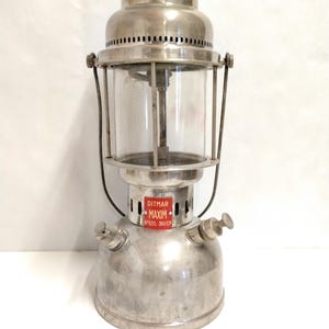 Könnte beinhalten: Vintage Ditmar Maxim Laterne mit rotem Deckel und klarer Glaskugel. Die Laterne hat einen silbernen Metallkörper mit einem Etikett "Ditmar Maxim N°520, 350 CP". Sie verfügt über zwei Knöpfe und einen Tragegriff.