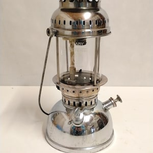 Könnte beinhalten: Eine verchromte Vintage-Laterne mit einer transparenten Glaskugel. Die Laterne hat einen Griff und einen Kraftstoffregler. Der Text "BABY" und "Petromax" ist auf dem Glas sichtbar. Die Laterne ist für den Außenbereich konzipiert.