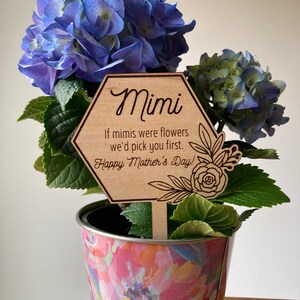 May include: A wooden plant stake with a hexagonal shape and the text "Mimi If mimis were flowers we'd pick you first. Happy Mother's Day!"  The stake is in a pot with a blue hydrangea plant.