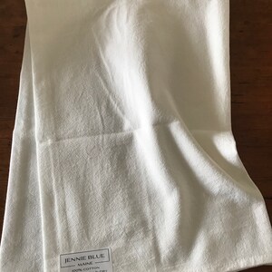 Pode incluir: Toalha de cozinha branca com uma etiqueta que diz "Jennie Blue Maine 100% Algod&atilde;o Lavar na m&aacute;quina e secar www.jennieblue.com"
