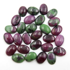 May include: A selection of oval gemstones in deep red, green, and purple hues. The polished stones are arranged on a white surface, highlighting their natural colour variations and textures. These gemstones are suitable for jewellery making.