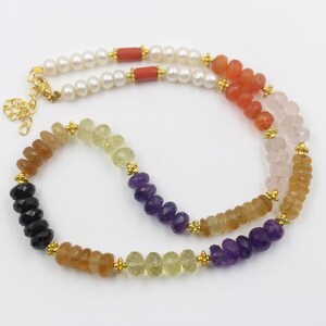 Può includere: Una collana a più fili con pietre preziose e perle colorate. La collana include perline nere, arancioni, gialle, viola e rosa, insieme a perle bianche e accenti di corallo rosso. Chiusure e connettori color oro completano il design.