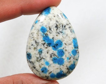 May include: A teardrop-shaped cabochon of blue kyanite in a white matrix. The stone has a speckled appearance with blue and white spots.