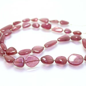 May include: A strand of pink gemstone beads, each bead is a smooth, oval shape with a slightly irregular edge. The beads are strung on a thin wire.