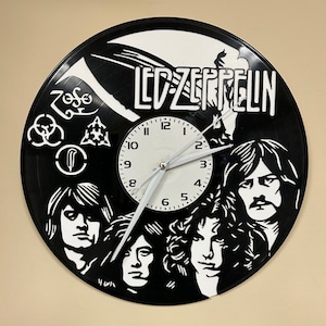 May include: A black vinyl record clock featuring a white silhouette of the band Led Zeppelin. The clock face is white with black numbers and hands. The band members' faces are visible in the silhouette.
