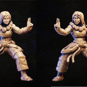 May include: A 3D printed figurine of a female warrior in a fighting pose. She is wearing a brown top, pants, and a belt with a rope. She has a fierce expression on her face and is holding a flaming weapon in each hand.