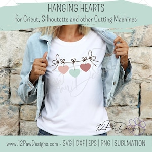 May include: A white t-shirt with a design of three pink and green hearts hanging from a string with bows. The text "HANGING HEARTS" is at the top of the image. The text "for Cricut, Silhouette and other Cutting Machines" is below the hearts. The text "12PawDesigns" is at the bottom of the image. The text "www.12PawDesigns.com - SVG | DXF | EPS | PNG | SUBLMATION" is at the bottom of the image.