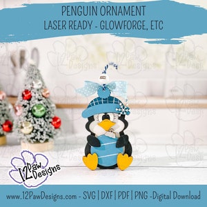 Pode incluir: Um enfeite de pinguim azul e branco com um chap&eacute;u azul e um floco de neve. O enfeite est&aacute; segurando uma bola azul e branca listrada. O enfeite est&aacute; pronto para laser para Glowforge, etc. O texto "2022" est&aacute; no enfeite.